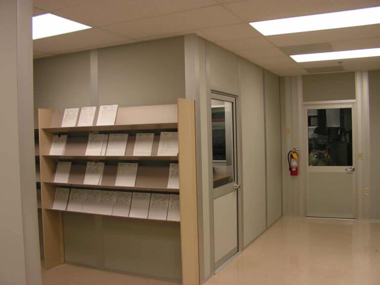A clean, well-lit office corner in the new wing of the hospital with a large shelf filled with neatly organized documents. There's a glass door on the right and a fire extinguisher mounted on