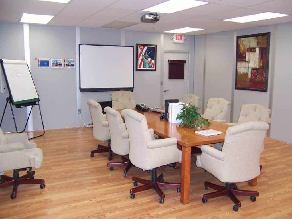 A modern boardroom with a large whiteboard, a flip chart, wheeled chairs arranged around a rectangular table, and various artworks on the walls, designed to achieve better communication.