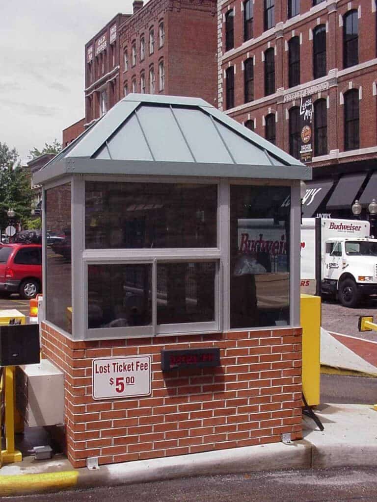 A parking management booth made of brick and glass, with a green pyramid-shaped roof. A sign on the booth reads 