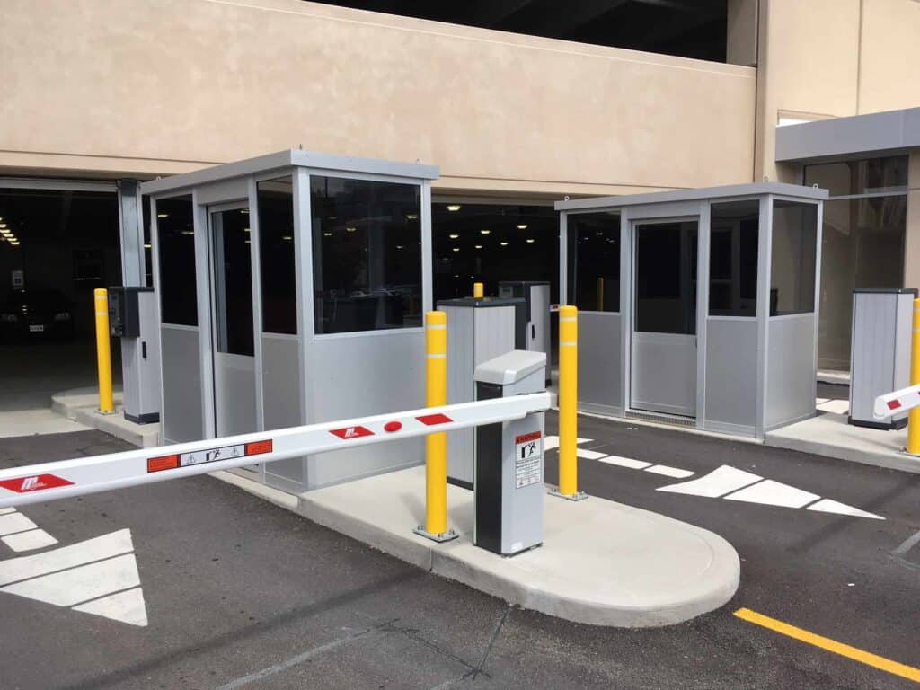 Two security booths with barriers at a parking garage entrance, featuring crosswalk markings on the pavement.