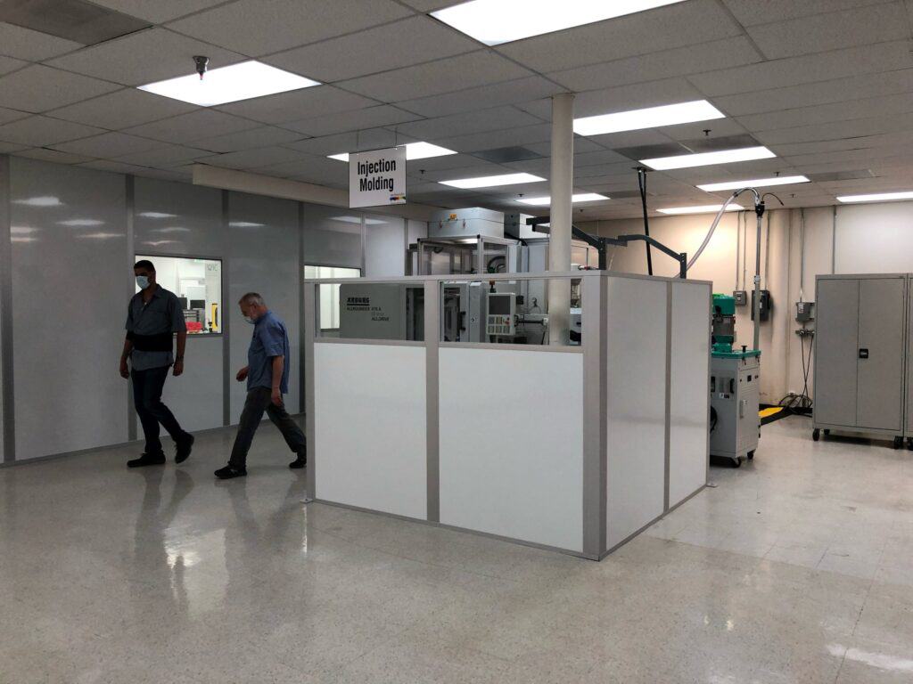 Two men walking through an industrial workspace with machines labeled 