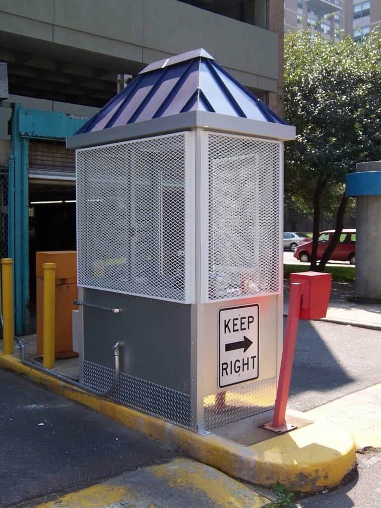 A security booth with a blue and white striped roof situated next to a yellow barrier with a 