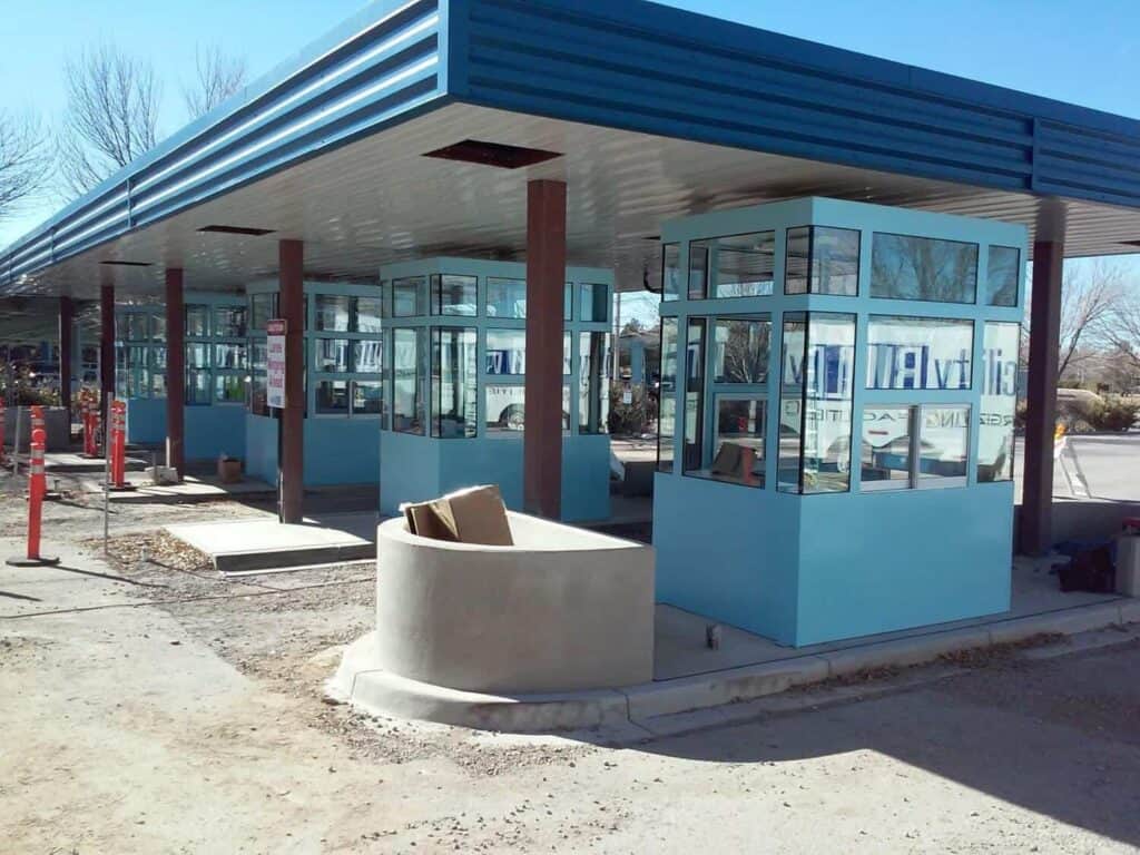 A modern bus stop with blue panels and large glass windows under a slanted roof, featuring a bench, trash can, and parking management solutions brochure stand, set against a sunny, clear sky.