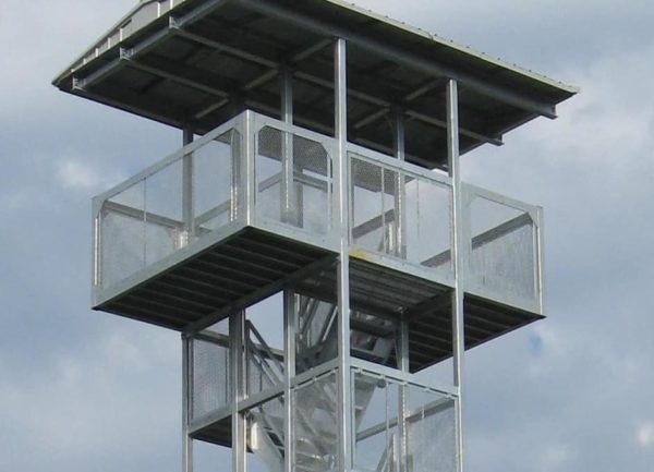 A close-up view of The High-Rise, a tall, metal observation tower with several platforms, surrounded by a light blue sky with scattered clouds.