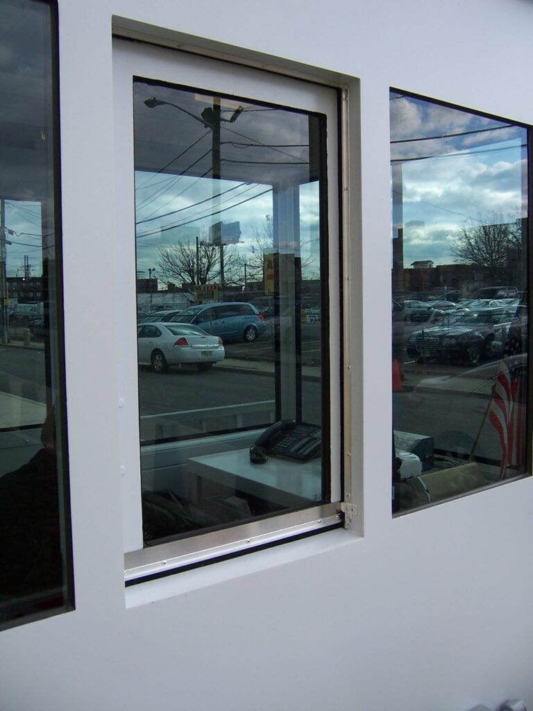 A reflection of a street and parked cars captured through an open sliding window framed by white trim, contrasting with a dark interior and adjacent closed windows.
