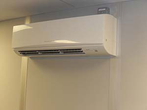A wall-mounted ductless air conditioning unit in a room, displaying a clean, contemporary design. The unit is in operation with visible vents, situated above door height on a neutral-colored wall.