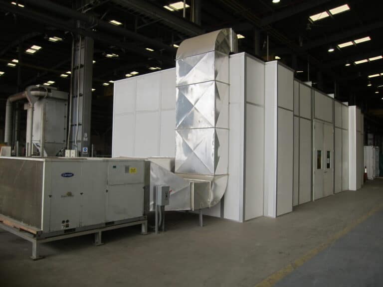 Large industrial cleanroom HVAC system inside a spacious factory, featuring metallic ducts and insulated panels, with various machinery units, under bright overhead lights.
