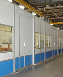 Gray and blue modular wall panels with glass sliding doors in an industrial setting, featuring overhead lighting.
