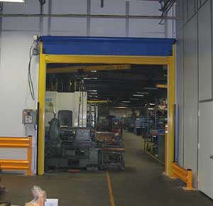 A view into an industrial warehouse through a large yellow roll up door, showing machinery and equipment scattered across the interior.