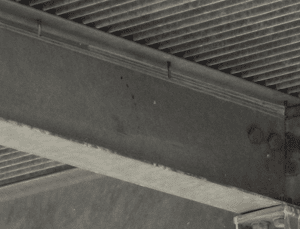 Close-up of dusty ventilation ducts and exposed beams in an industrial setting, showing signs of wear and lack of maintenance.