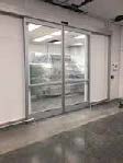 Automatic sliding doors opening to a room with visible interior lights and shelves, set in a wall with white and gray tones, viewed across a glossy tiled floor.