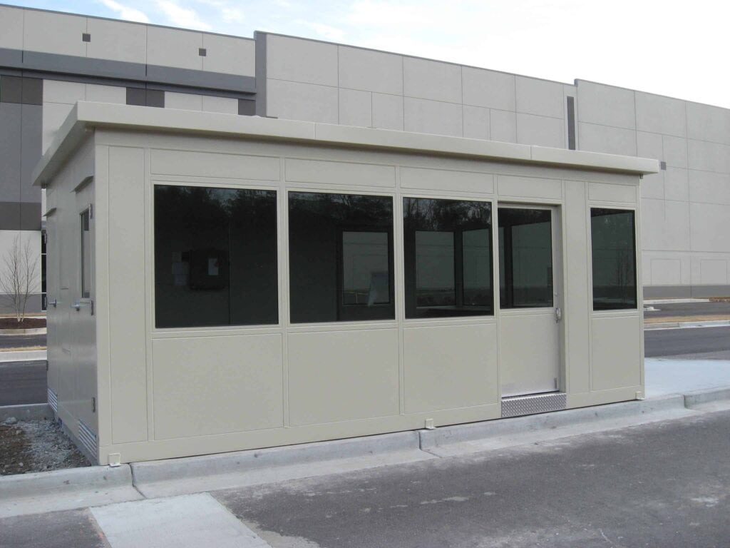 Guard/Security Booth 41 A beige security booth with large windows and a single door, located outside a building with a gray facade.