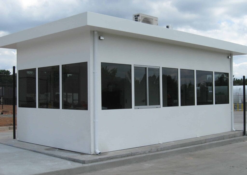 Guard/Security Booth 33 A small, modern, white prefabricated security booth with a flat roof and large windows on three sides, situated on a concrete base in a clear area.