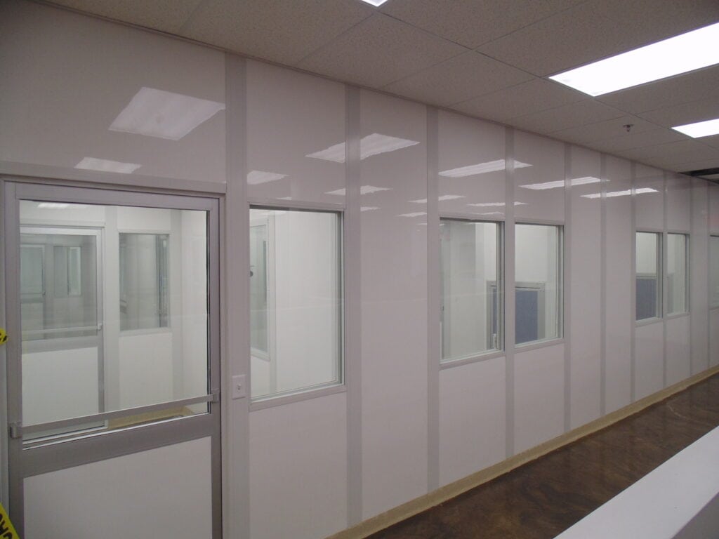 Interior view of a modern office corridor with modular walls, featuring doors and reflective ceiling lights. Neutral colors dominate the space.