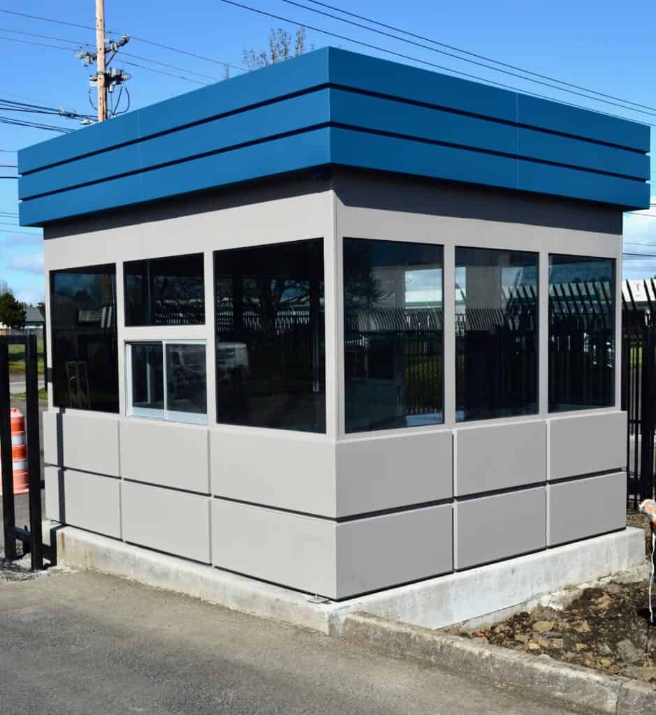 Guard/Security Booth 44 A small, modern security booth with blue trim is positioned near a gated area. The booth has large windows on all sides, providing visibility of the surrounding area.