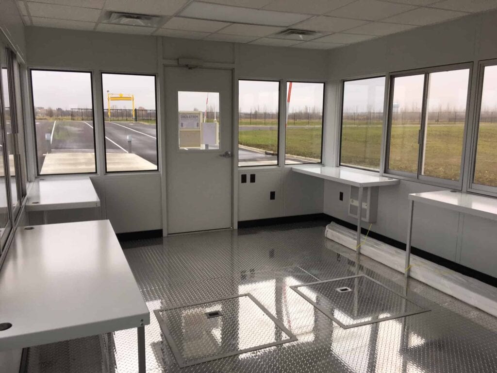 Guard/Security Booth 38 Interior of an empty, modern security booth with large windows, built-in counters, and cabinets, viewed on a cloudy day. The design features a black and white color scheme, enhancing its clean, functional