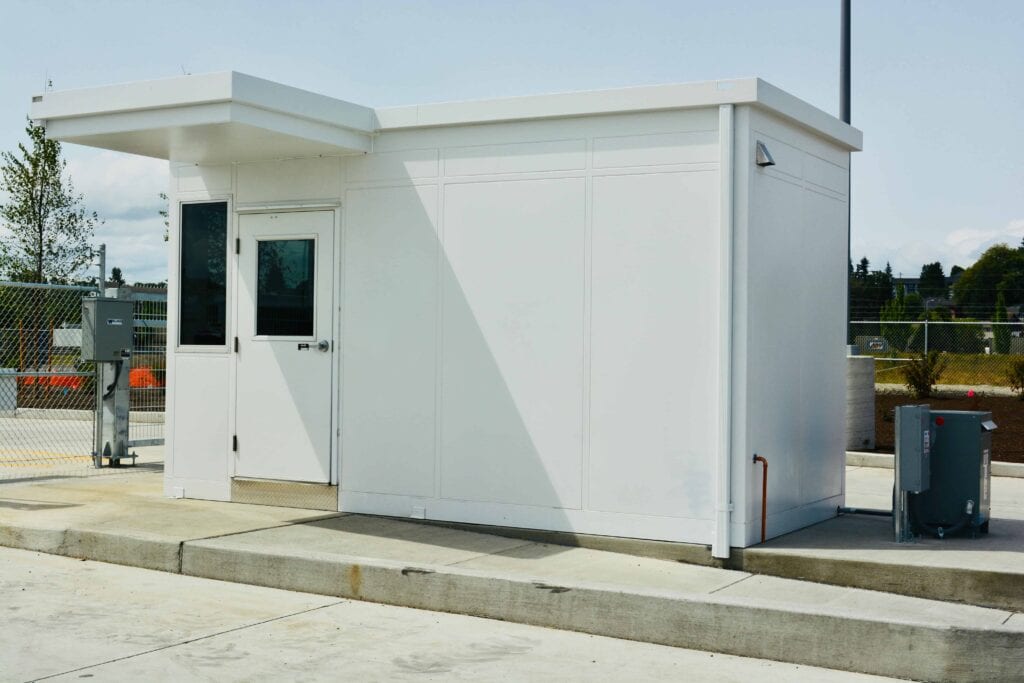 Guard/Security Booth 51 A modern white safety booth with a small roof extension, featuring a door and a window, located on a concrete platform under a clear blue sky.