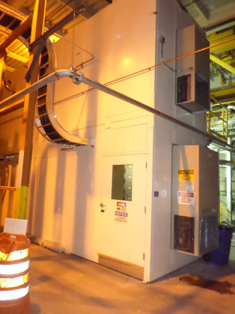 Motor Control Center Enclosure 4 Large industrial Motor Control Center in a facility with caution and notice labels, connected by various pipes and cables, near a traffic cone.