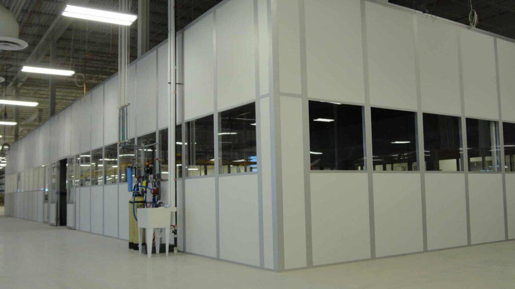 A well-lit, modern industrial facility with clean white walls and large windows partitioning different sections inside the space. A variety of indoor equipment enclosures stand by the transparent panels.