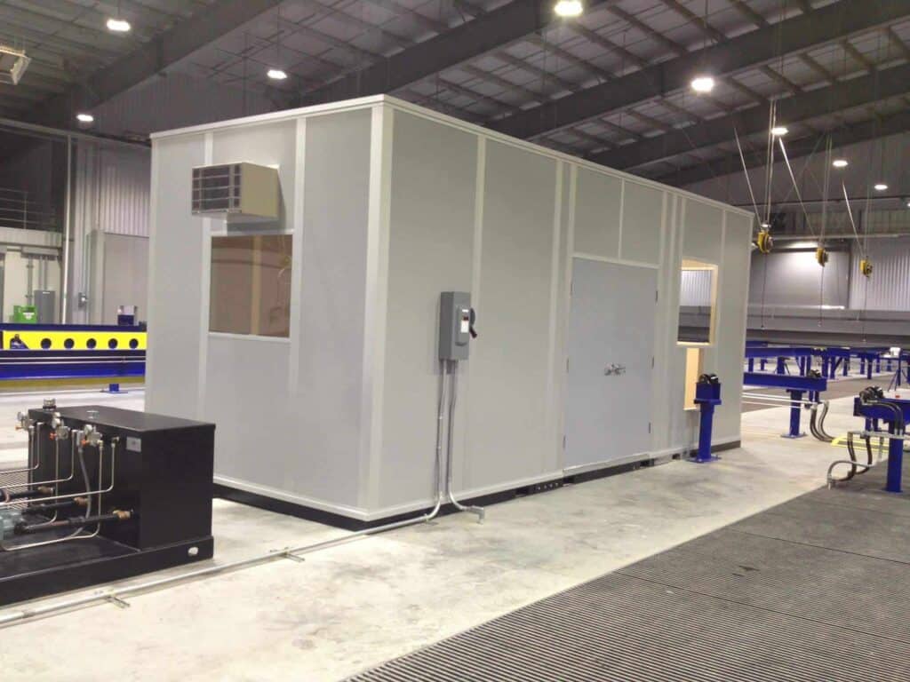 A large gray industrial modular container with various equipment and a small air conditioning unit, positioned inside a spacious factory with blue accents as an indoor equipment enclosure.