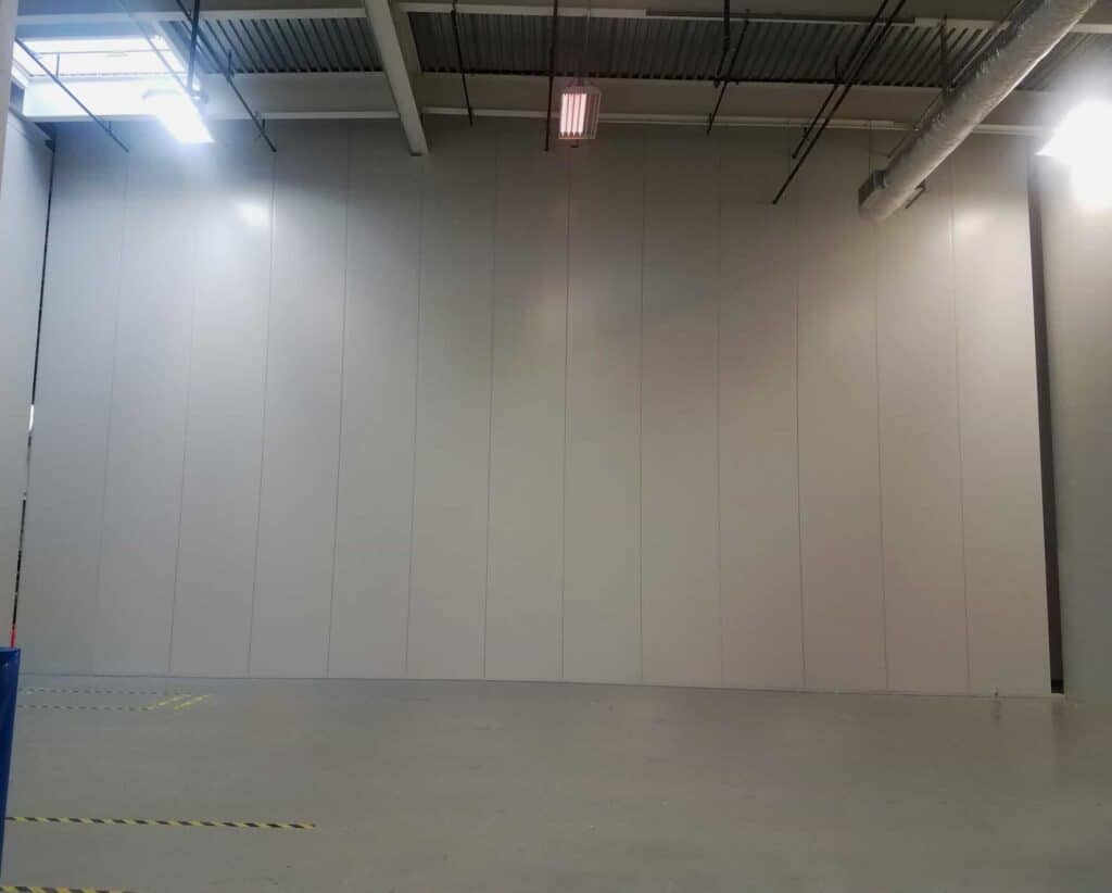Tall Modular Wall White 8 An empty industrial space with gray modular tall walls, ceiling-mounted lights, and visible hvac ducts, with a visible safety marking on the floor near the corner.