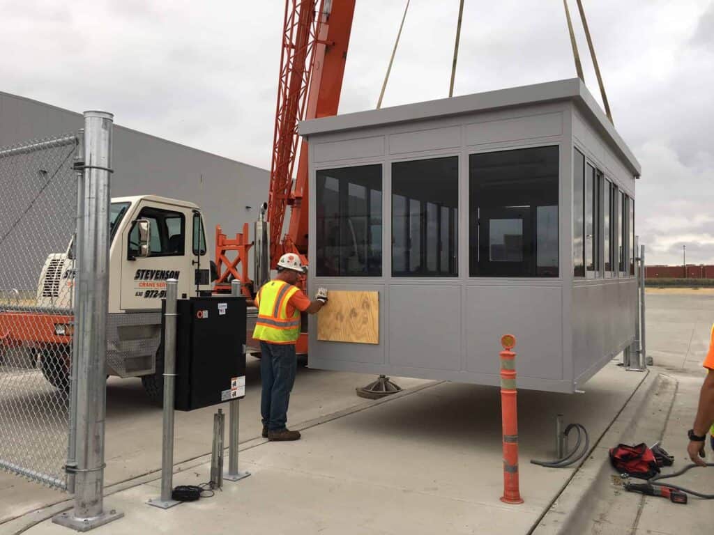 Guard/Security Booth 36 Construction workers using a crane to install a prefabricated security booth at a construction site.