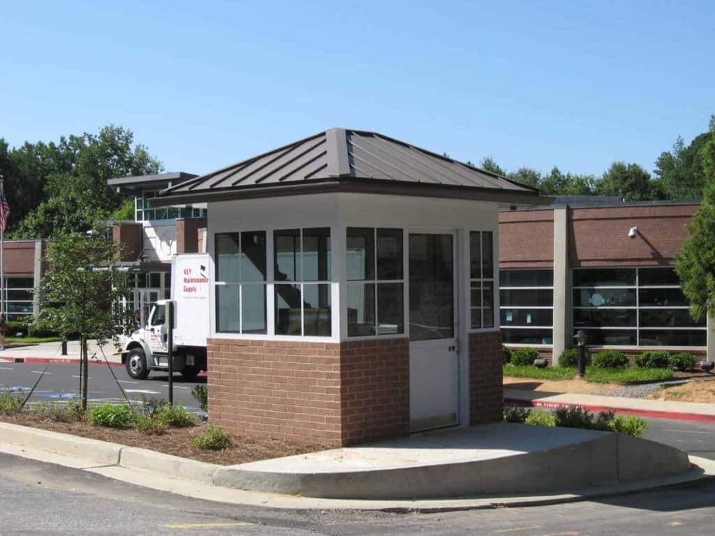 Guard/Security Booth 11 Small security booth at the entrance of a parking lot, with a white security truck parked nearby. The building has large windows and a pyramid-shaped roof.