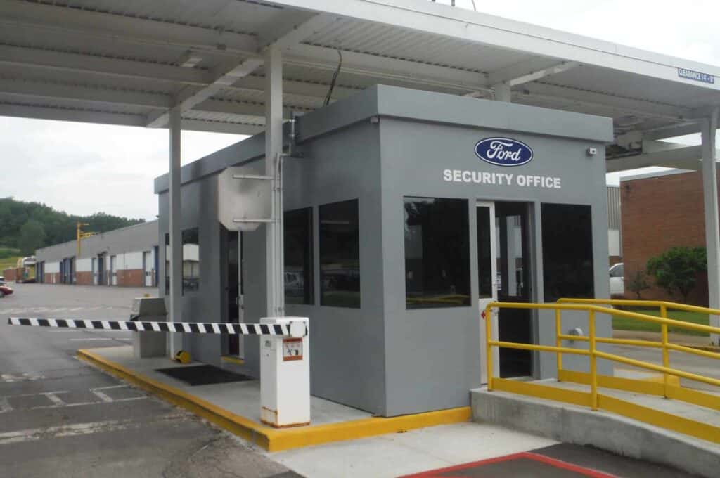 Guard/Security Booth 22 A security booth at a ford facility with a barrier gate, under a covered entrance, featuring the ford logo on the facade of the building.