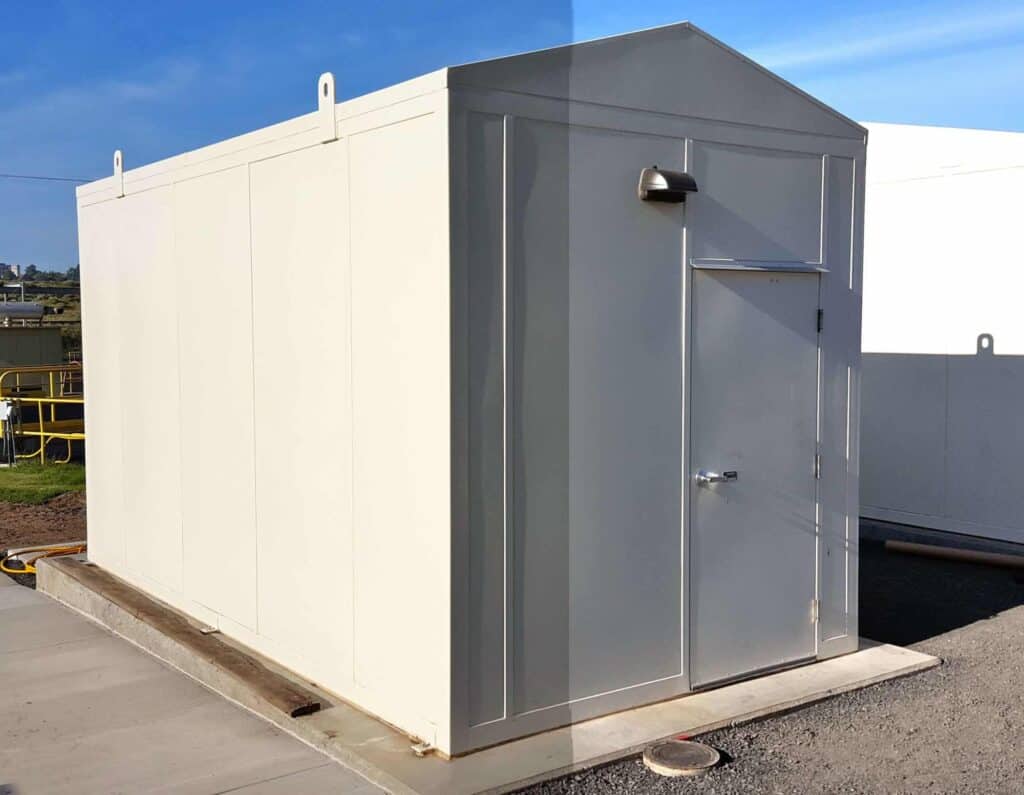 A standalone gray metal utility shed with a single door, positioned on a concrete base in an outdoor area with a clear blue sky, serving as one of the outdoor enclosures.